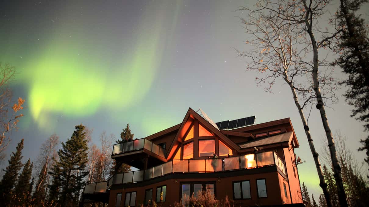 The timber roof of an aurora lodge near Madeline Lake under a pale green aurora