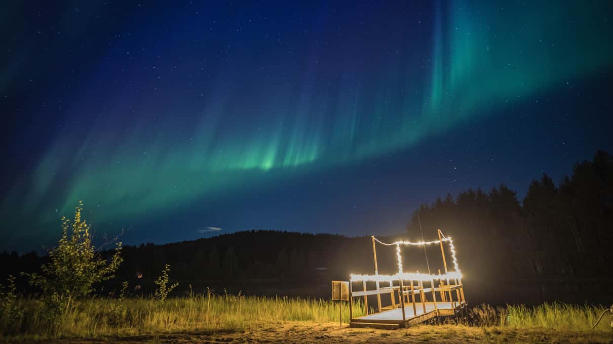 Green aurora glowing over a frozen forest lake near Rovaniemi on a clear winter night