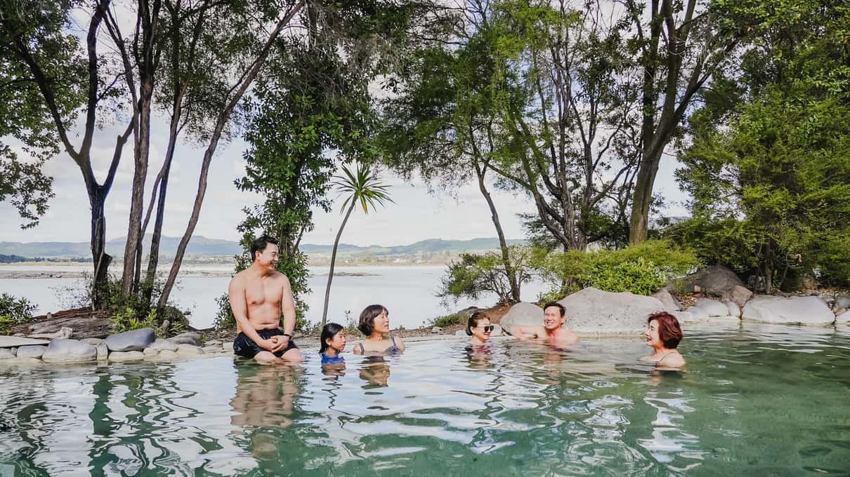 Bathers sitting in rock-lined mineral pools at the edge of Lake Rotorua
