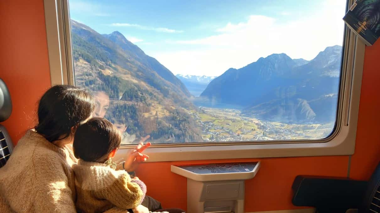 A child at the open window of the red Bernina train looking out over an alpine valley