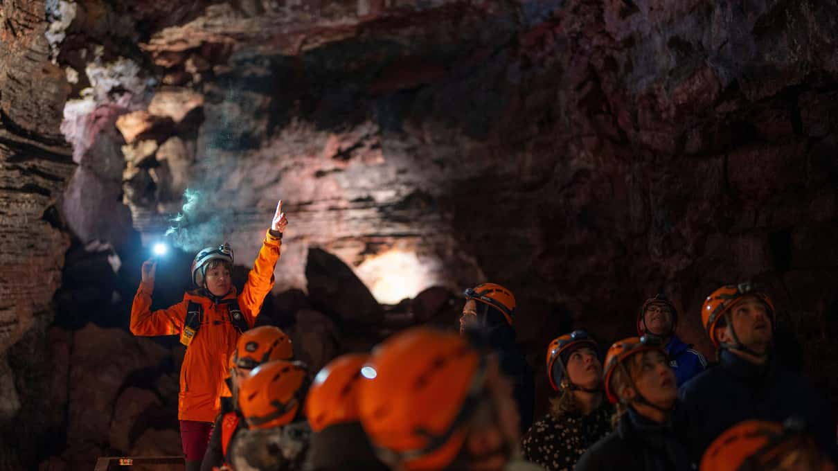 A group in helmets and head torches inside a lava tube cave with reddish mineral walls