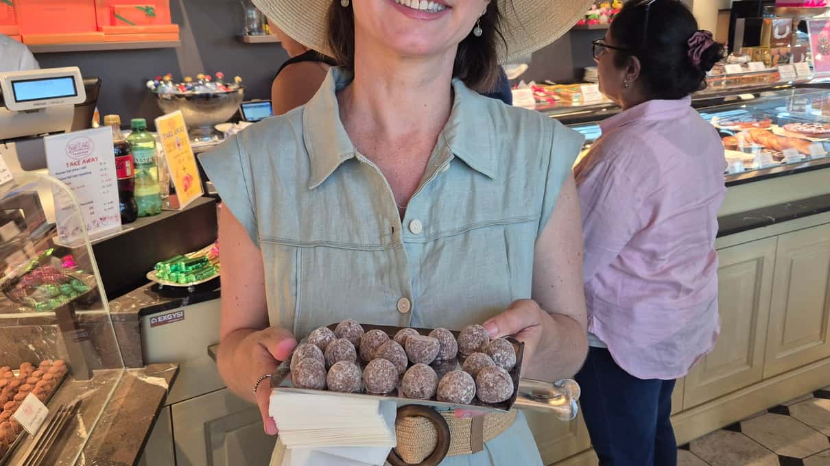 A smiling chocolate tour guide in a straw hat standing in front of the counters of a Zurich chocolate shop