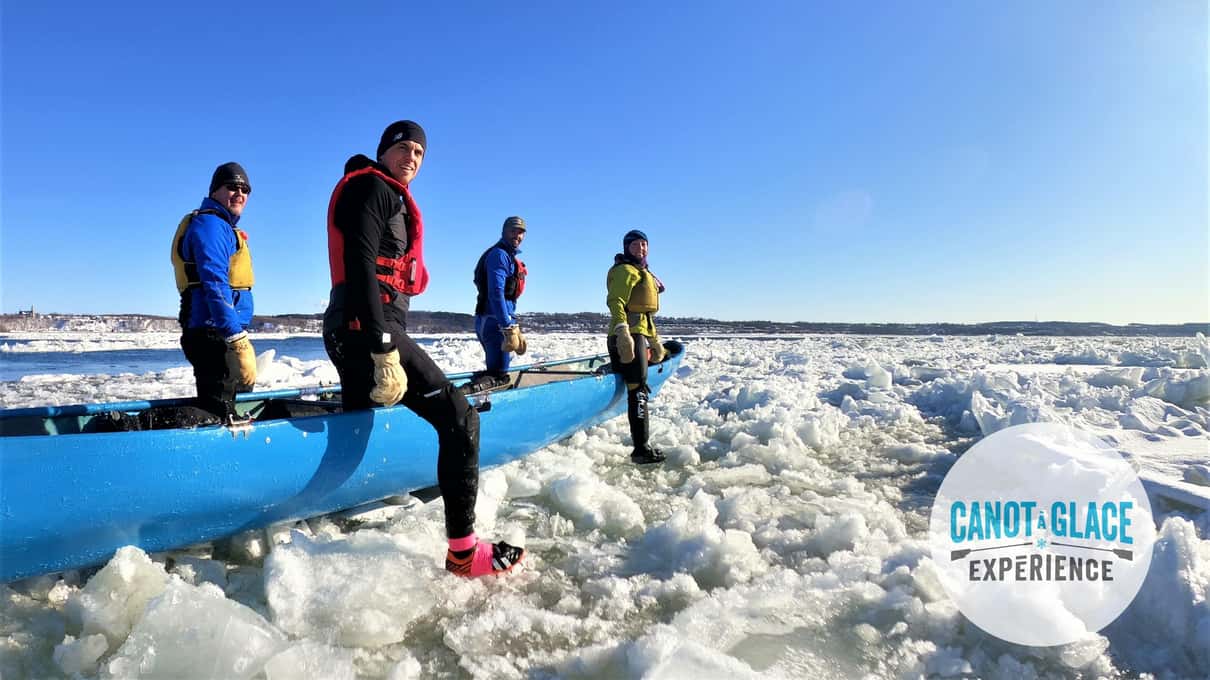A team in bright jackets pushing a long blue canoe across broken ice on the St Lawrence River