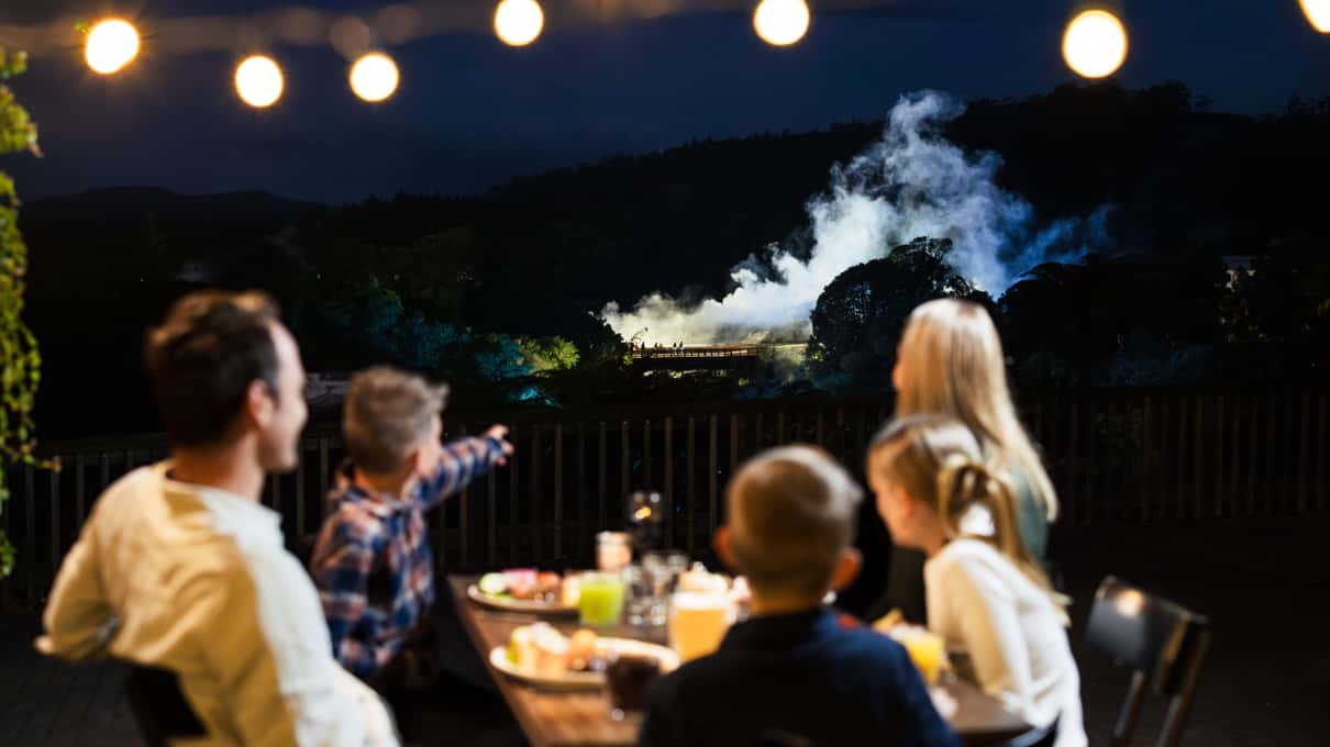 Visitors standing on the geyser terrace at Te Puia at dusk as steam drifts across the valley