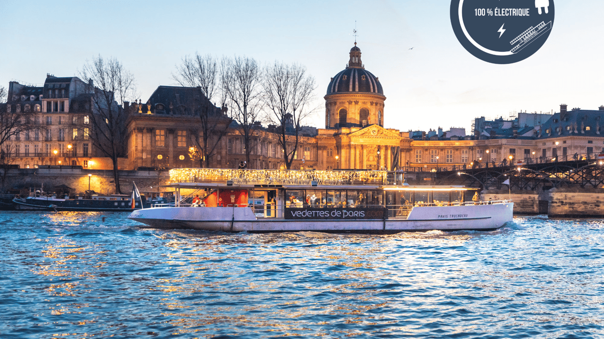 Beleuchtetes Ausflugsboot auf der nächtlichen Seine vor dem Institut de France
