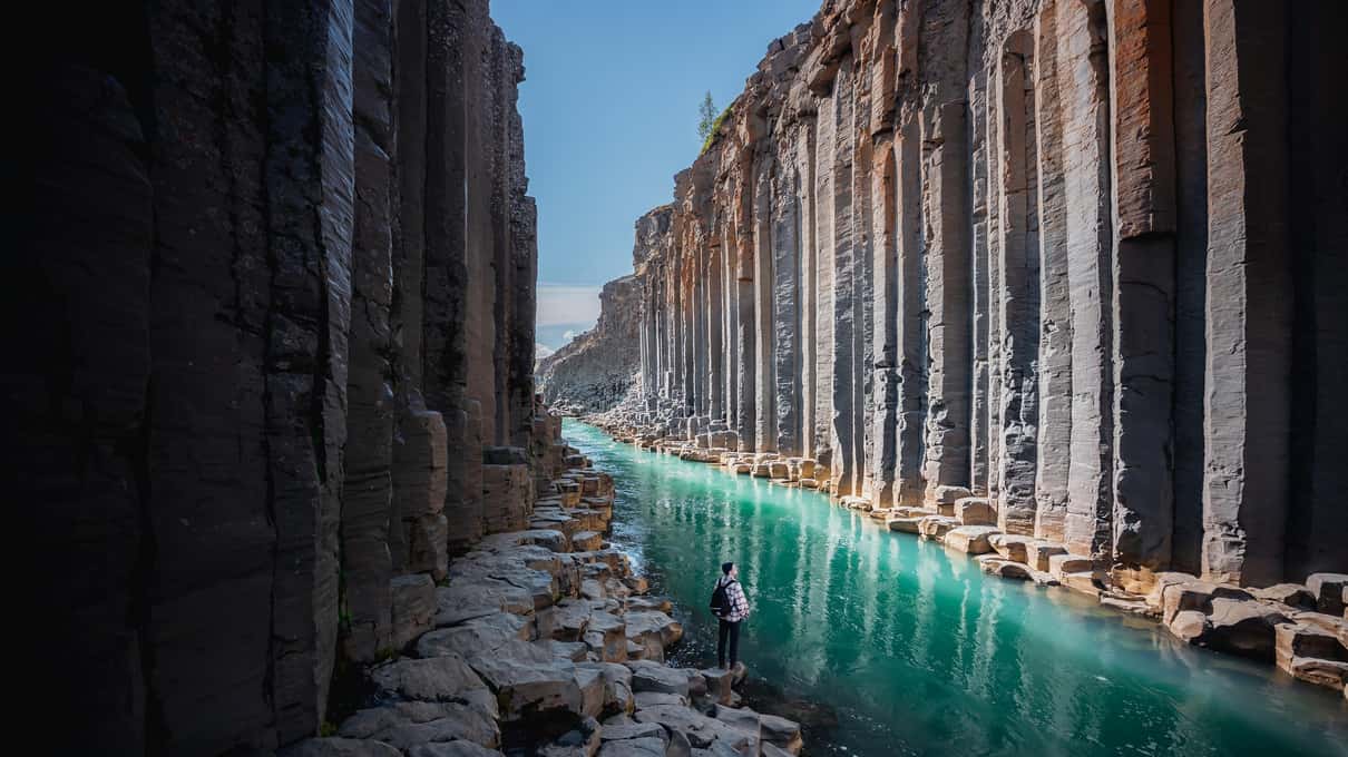 The narrow canyon floor with turquoise water running between two dark walls of basalt columns