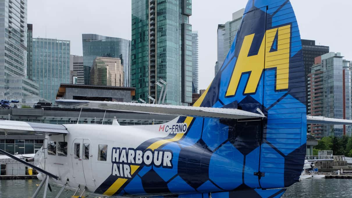 The blue and yellow tail of a Harbour Air floatplane tied up at the Coal Harbour dock below downtown glass towers