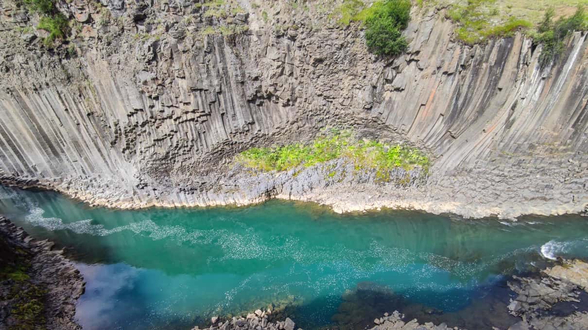 Walls of basalt columns curving around a turquoise pool in the river at Stuðlagil