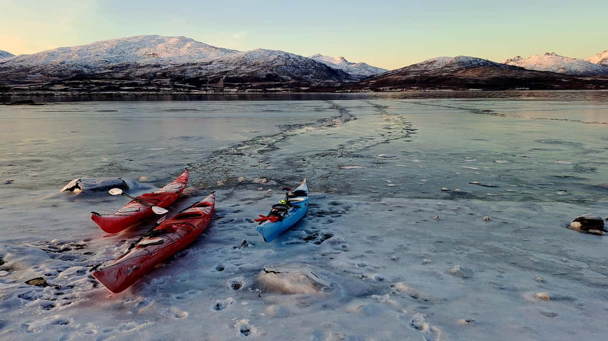 Three sea kayaks pulled up on an icy shore near Tromsø with frozen water at the edge