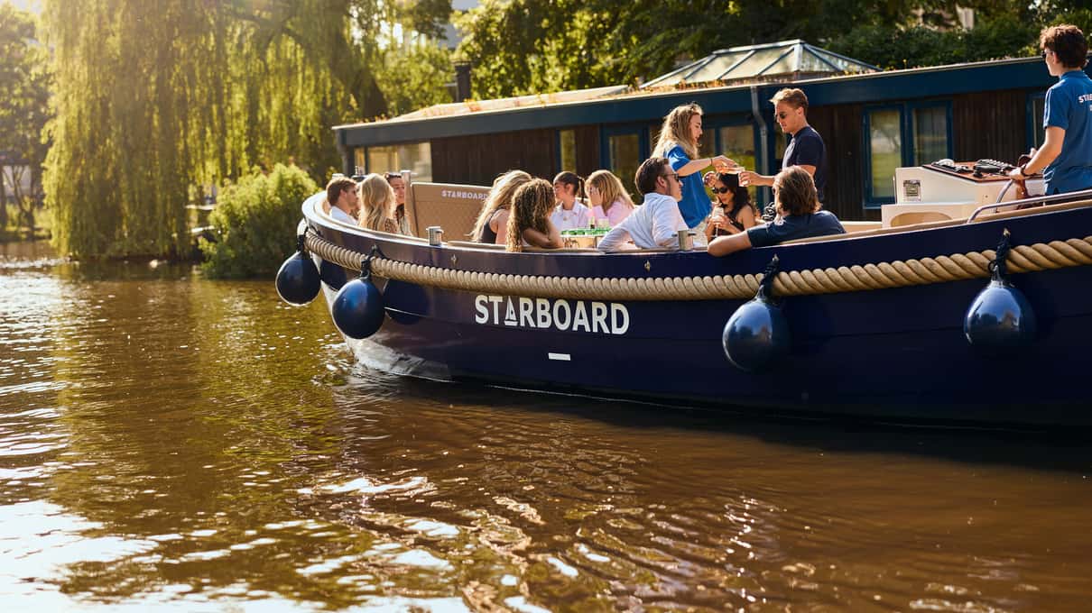 Barco abierto azul de Starboard con pasajeros navegando por un canal bajo sauces