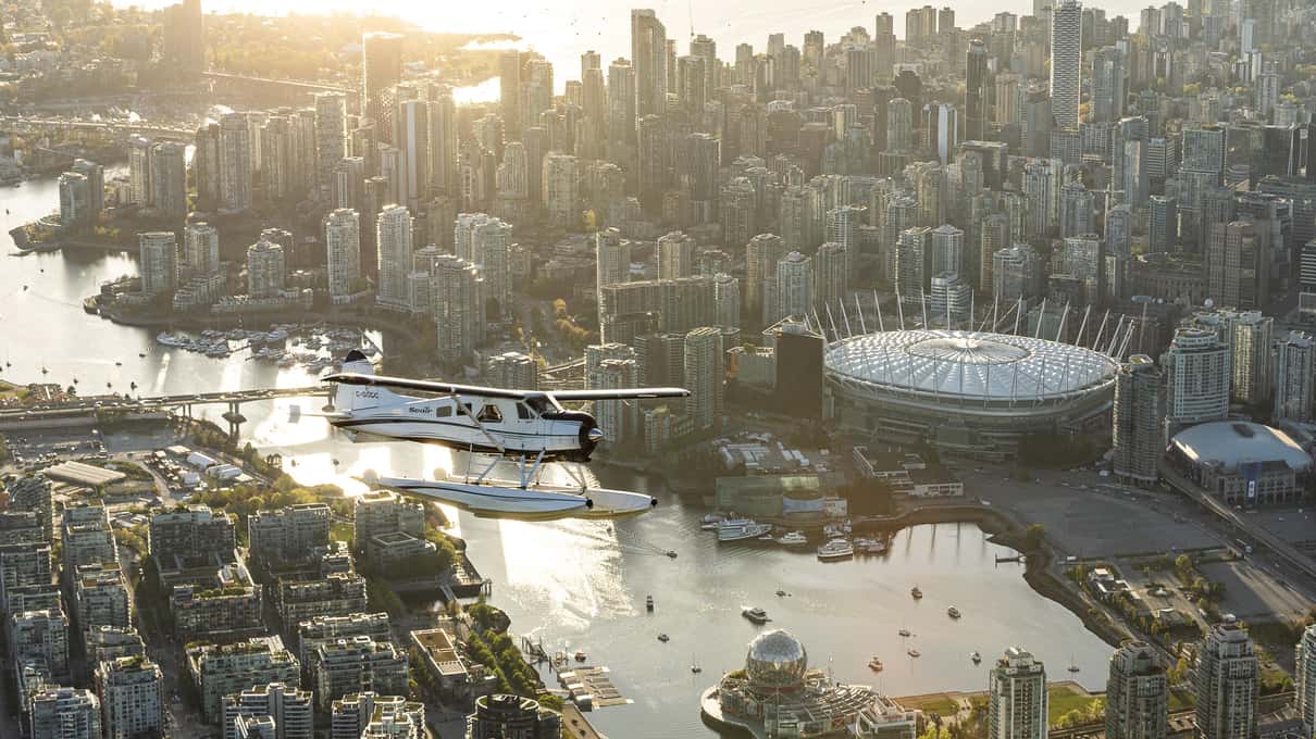 Seair Beaver floatplane flying over False Creek and the white roof of BC Place in golden evening light