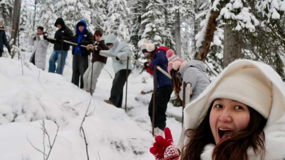 A smiling hiker in a white hat in front of a line of walkers on a snowy forest trail