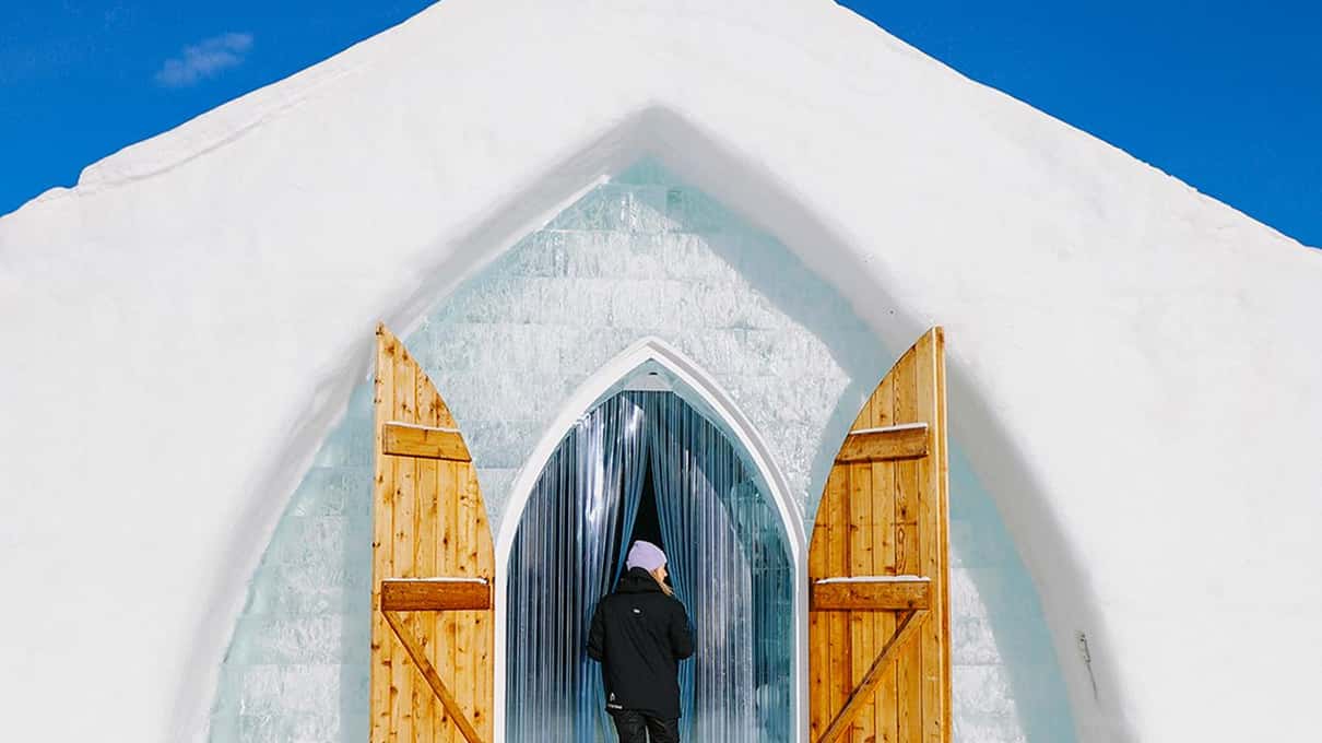 A visitor walking through the open wooden doors of the Hôtel de Glace into a pointed arch of ice