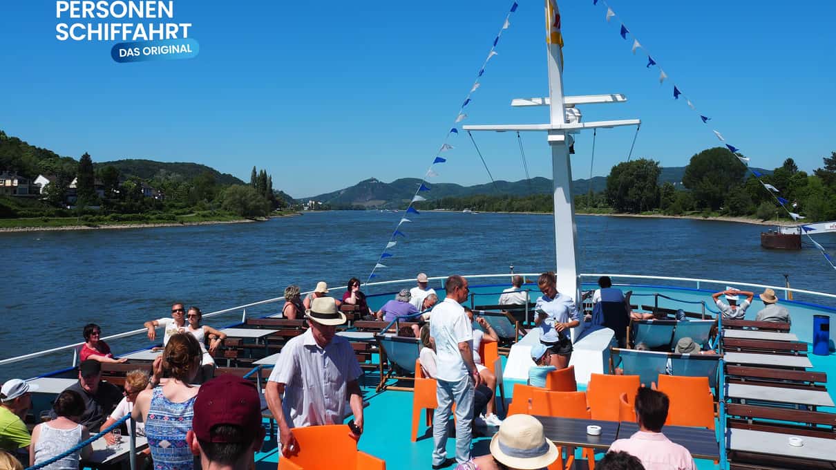 Passengers relaxing in the sun on the open upper deck of a sightseeing boat leaving Bonn