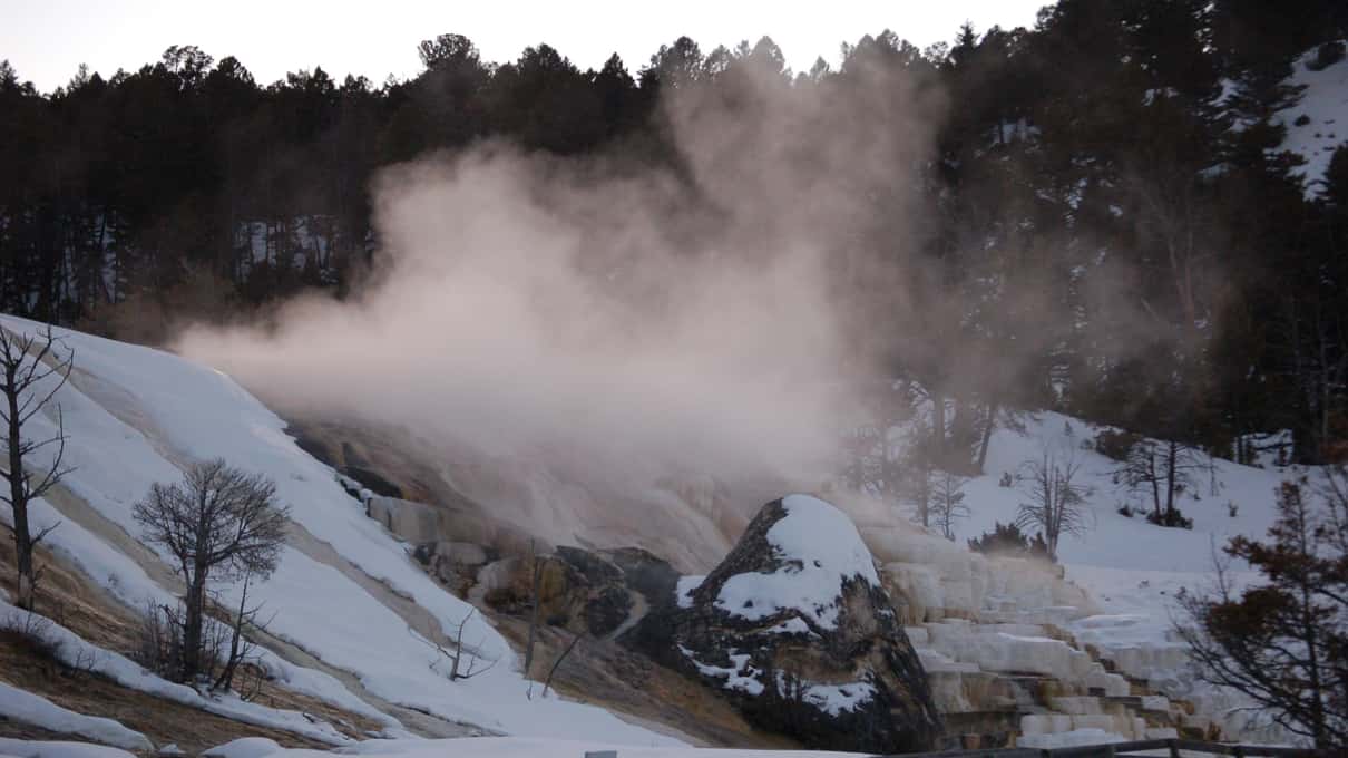 Steam rolling over a wooden boardwalk and snowy thermal terraces on a grey winter day