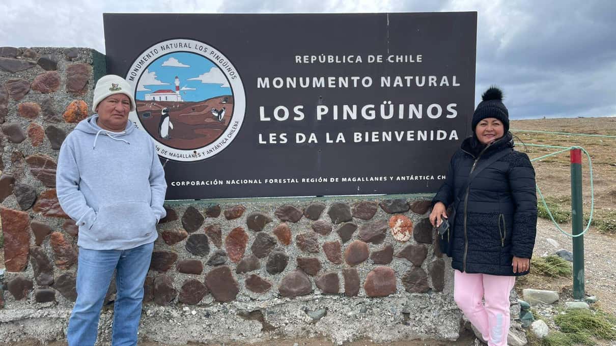 Visitors in hooded winter jackets gathered beside the Los Pingüinos Natural Monument sign on the island