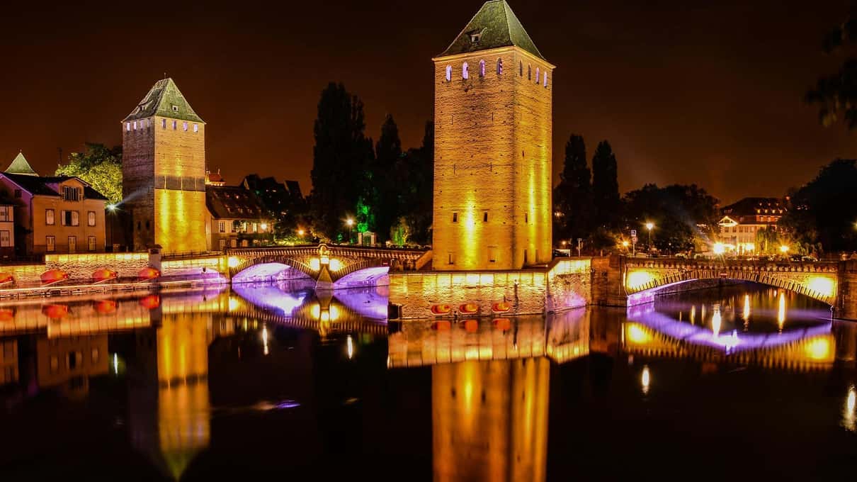 The medieval towers of the covered bridges lit up at night and reflected in the dark river below