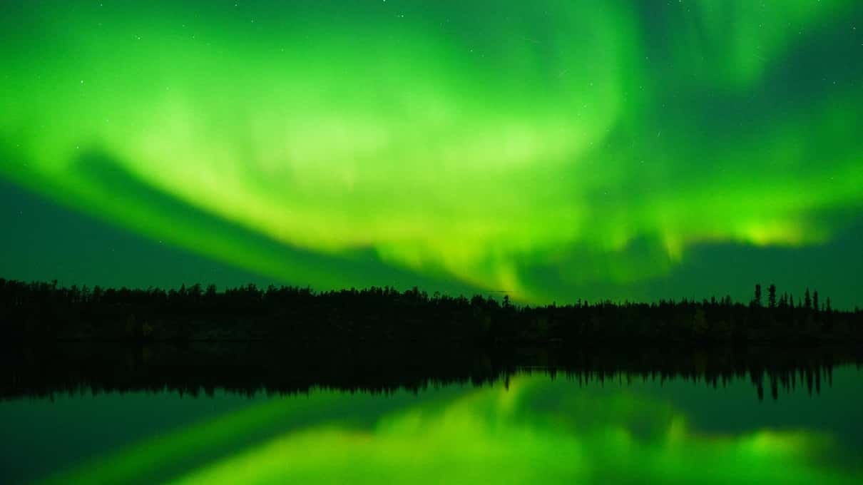 A bright green aurora arc hanging low over a dark horizon outside Yellowknife