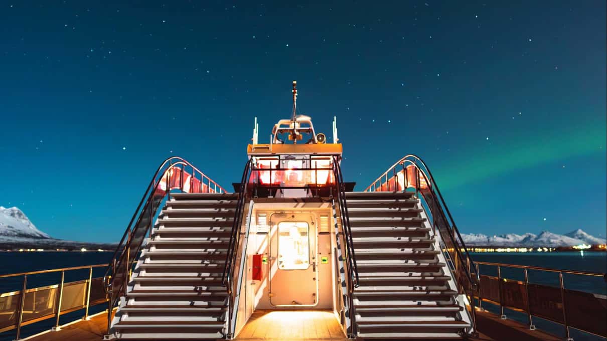 The lit bow and stairs of Brim's white boat under a starry sky with a faint aurora
