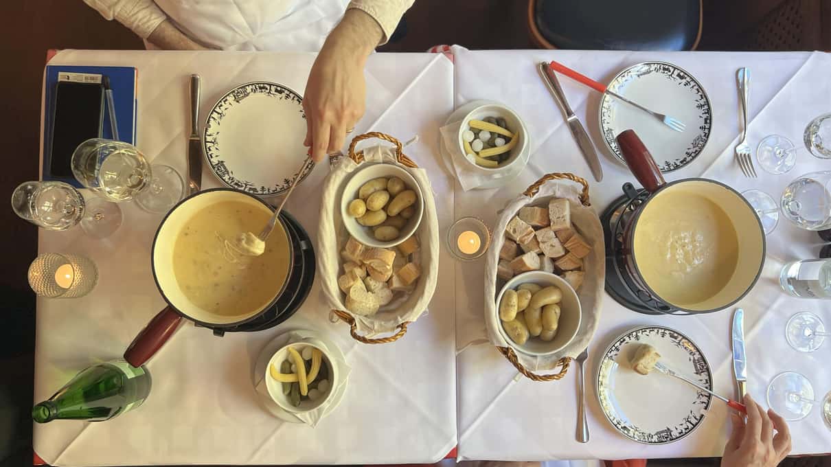 A table seen from above with a fondue pot, plates of golden Rösti and small dishes of Swiss specialties
