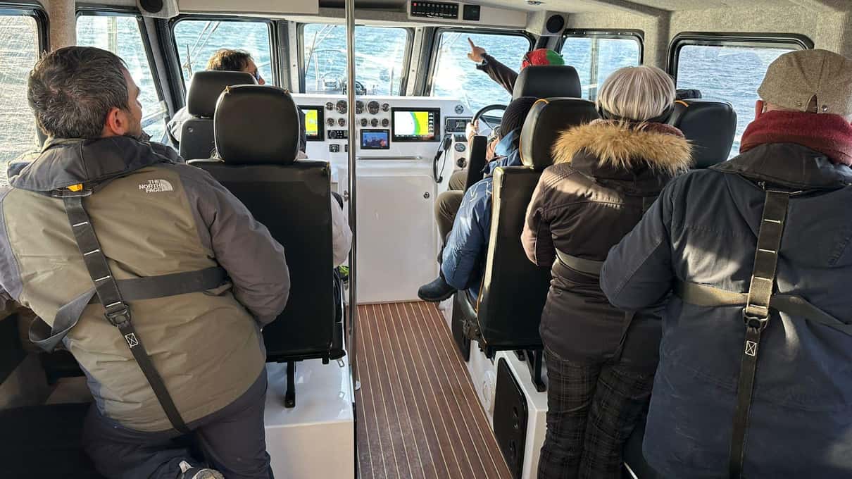 Guests in winter coats seated inside the heated cabin of a small whale watching boat
