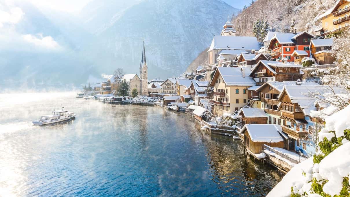 Hallstatt under snow, with its church spire and wooden houses above the lake and a small boat on the water