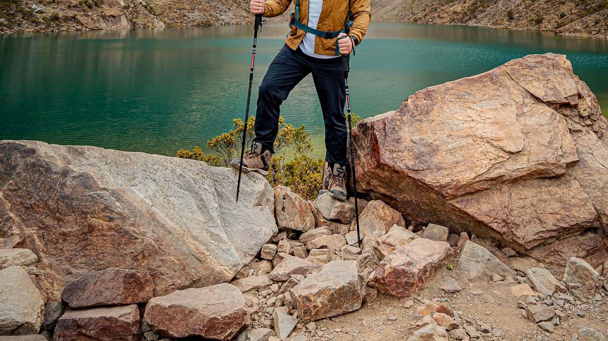 A hiker standing on a boulder high above the turquoise lake with cloud on the peaks