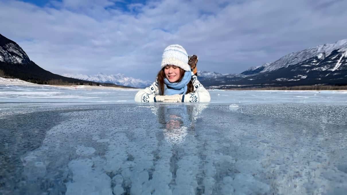 A woman lying on clear Abraham Lake ice above tall columns of stacked white bubbles