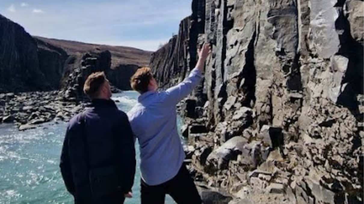 Two visitors in rain jackets looking down at the basalt columns from the edge of Stuðlagil canyon