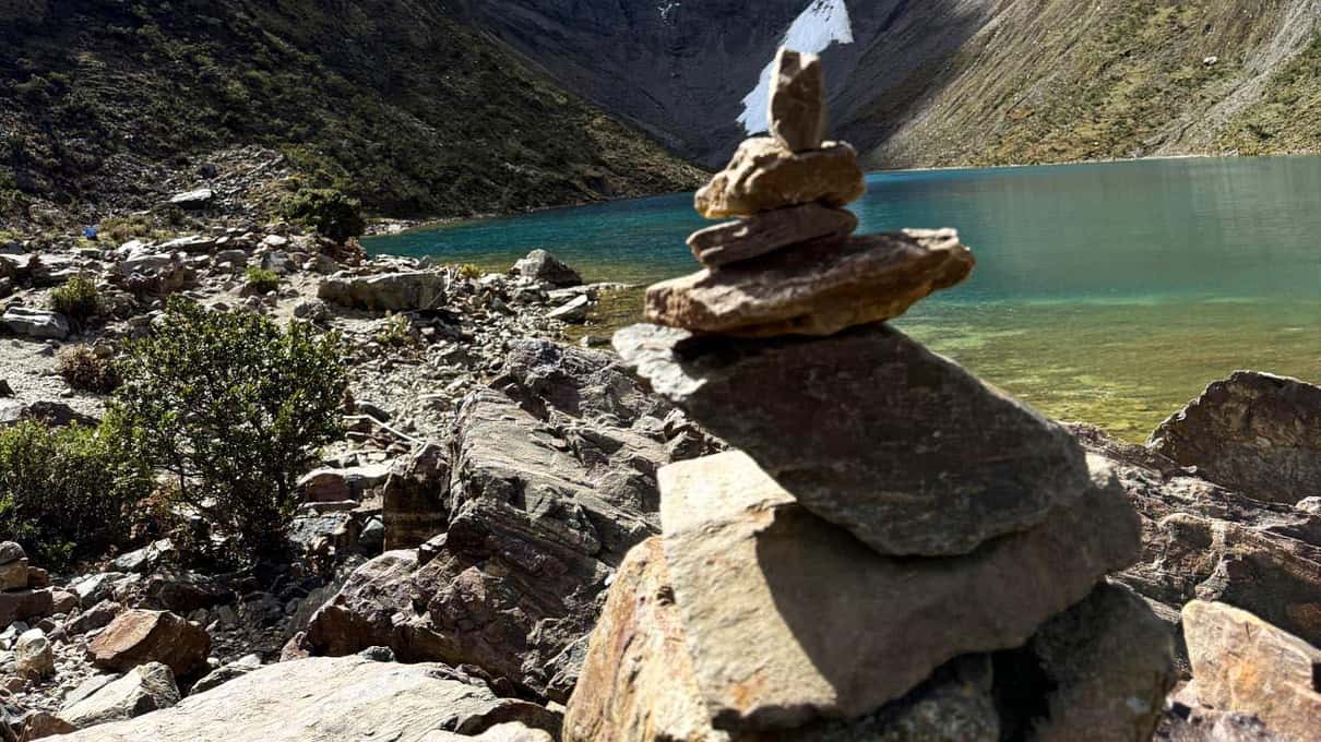 A stone cairn built on the rocky lakeshore with the glacier lake and icy slopes behind it
