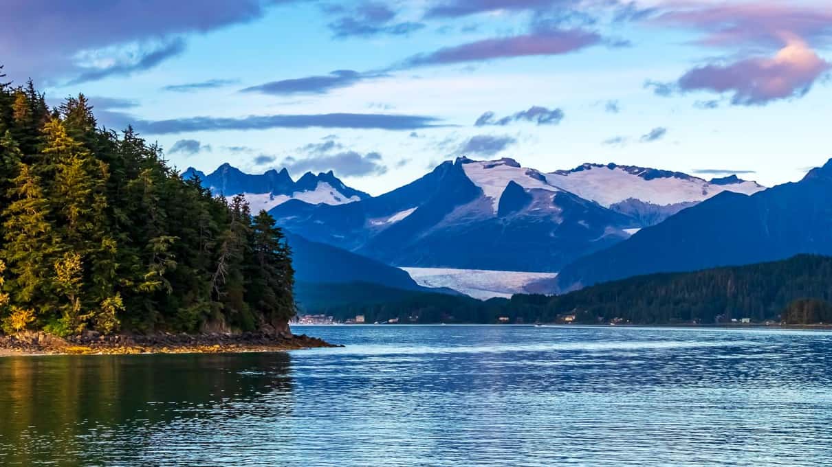 Un canal tranquilo cerca de Juneau con una isla cubierta de píceas y picos nevados a la luz dorada de la tarde