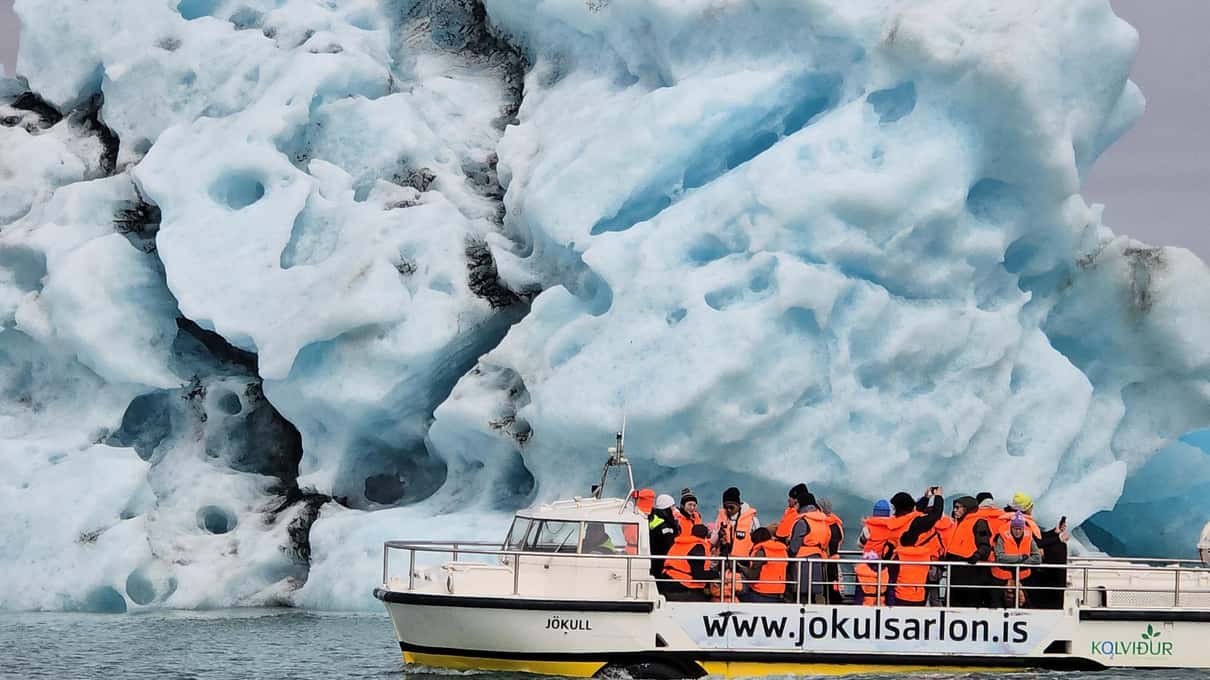 Amphibian boat full of passengers sailing past a towering blue iceberg on Jökulsárlón glacier lagoon in Iceland