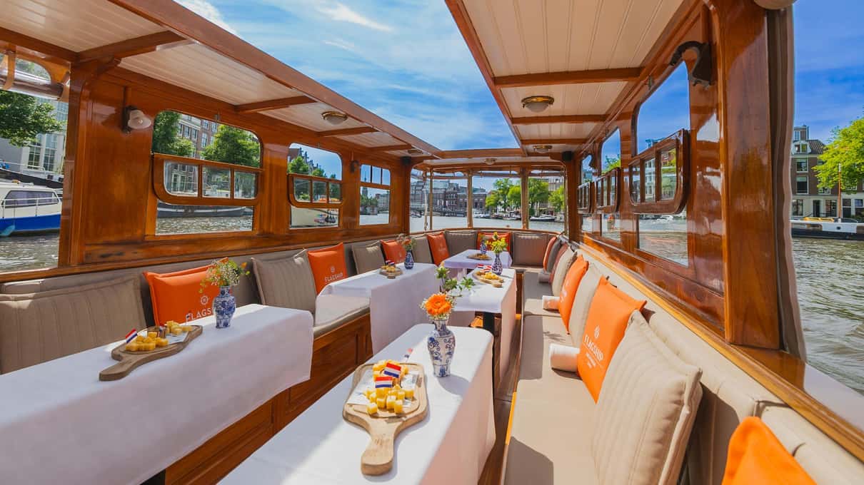 Houten interieur van een klassieke Amsterdamse salonboot met gedekte tafels en uitzicht op de gracht