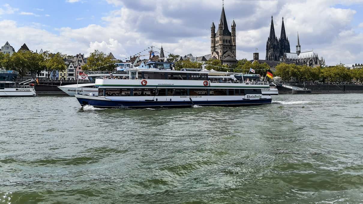 A white sightseeing ship on the Rhine in Cologne with the twin spires of the cathedral behind it