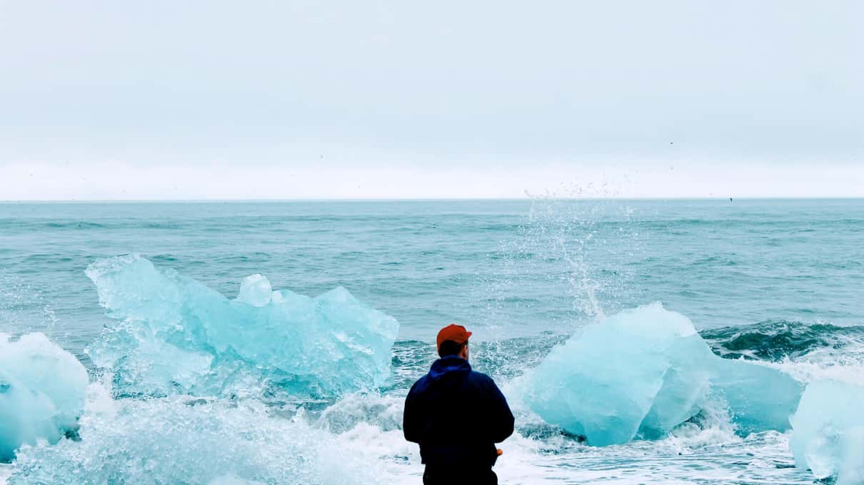 Visitor watching waves break over glacier ice on the black sand shore beside Jökulsárlón