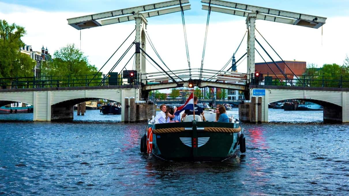 Łódź Eco Boats z pasażerami przepływa pod białym zwodzonym mostem Magere Brug na rzece Amstel