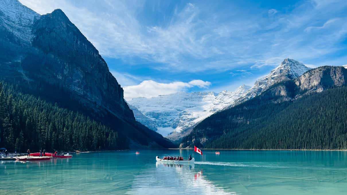 Turquoise Lake Louise with red canoes on the water and a glacier between the peaks