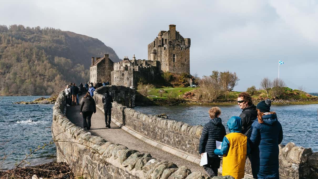 Visitors crossing the curved stone causeway to Eilean Donan Castle on its island at the head of Loch Duich