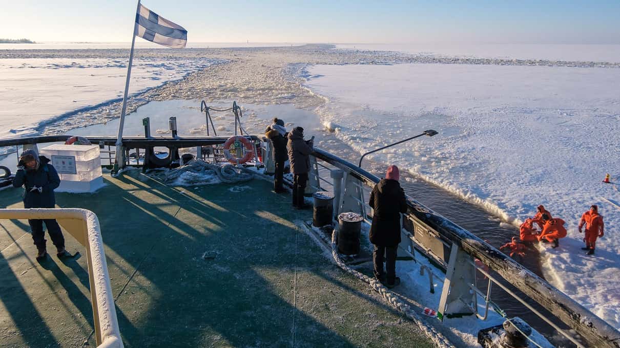 Guests standing on the green foredeck of Sampo looking out over the frozen sea in low winter sun