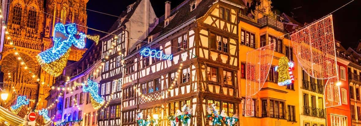 Half-timbered house fronts hung with large glowing angel lights on a dark winter evening