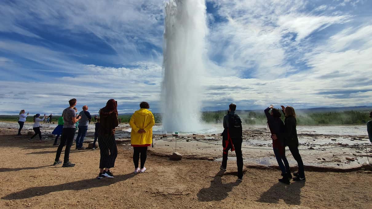 Strokkur geyser erupting while visitors in jackets watch from the path