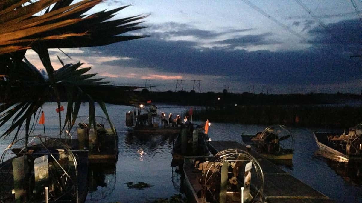 Airboats moored at a wooden dock under a dusky blue sky before the night ride
