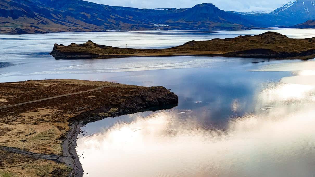 A still pool on the Hvammsvik shore mirroring the sky and the far hills