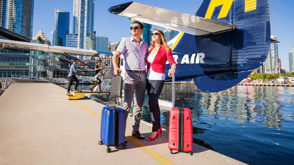 Couple with two rolling suitcases on the floatplane dock beside a blue and yellow Harbour Air tail