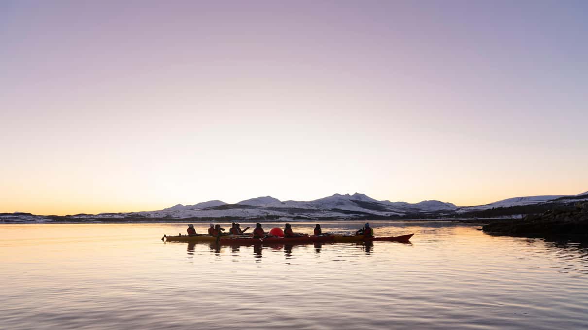Kayakers walking along a Kvaløya shore in silhouette against a low winter sunset