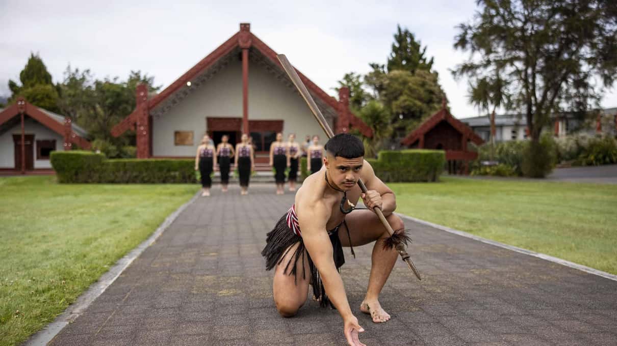 A warrior crouching low on the path to deliver the wero challenge during a welcome at Te Puia