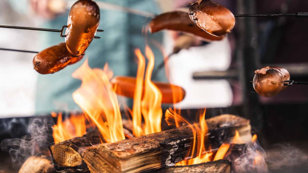 Sausages on wooden sticks grilling over a campfire during a Korouoma winter hike