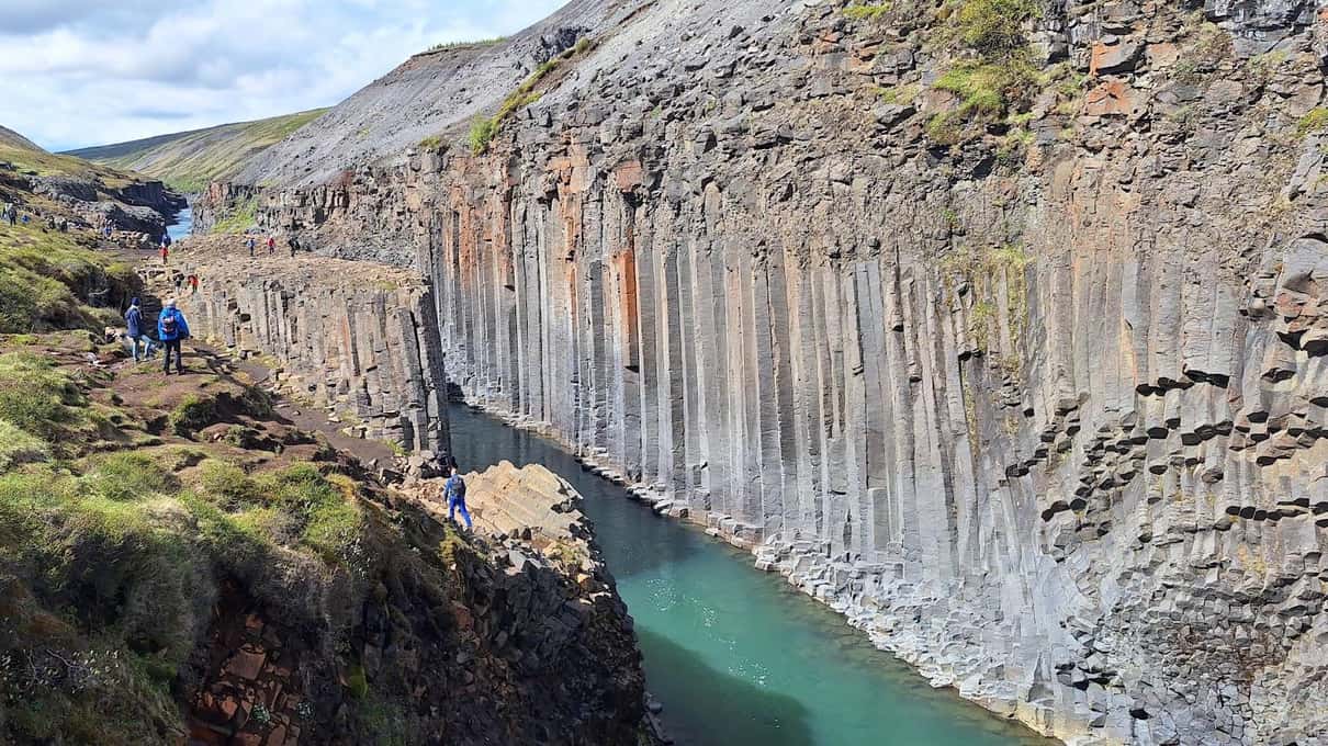 Walls of basalt columns rising above the turquoise river, seen from the green rim of the canyon