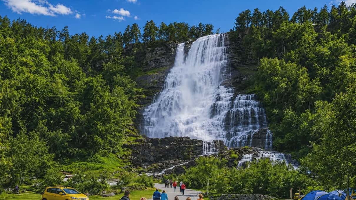 The multi-stranded Tvindefossen waterfall spilling down a mossy rock face in dense green forest