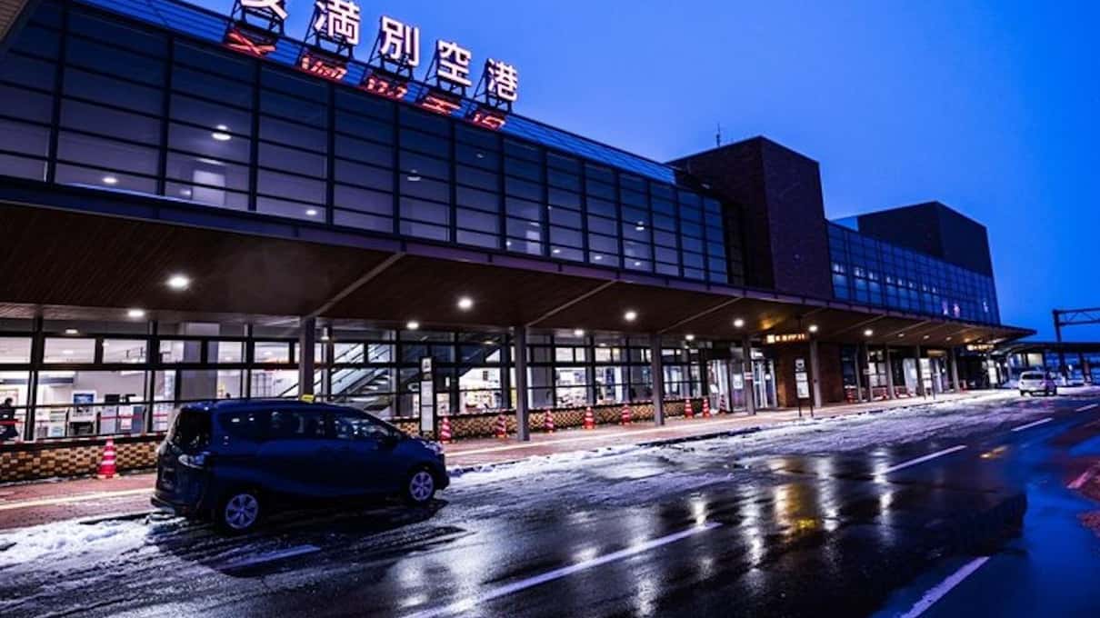 Memanbetsu Airport terminal lit up at dusk with its name in Japanese on the roof